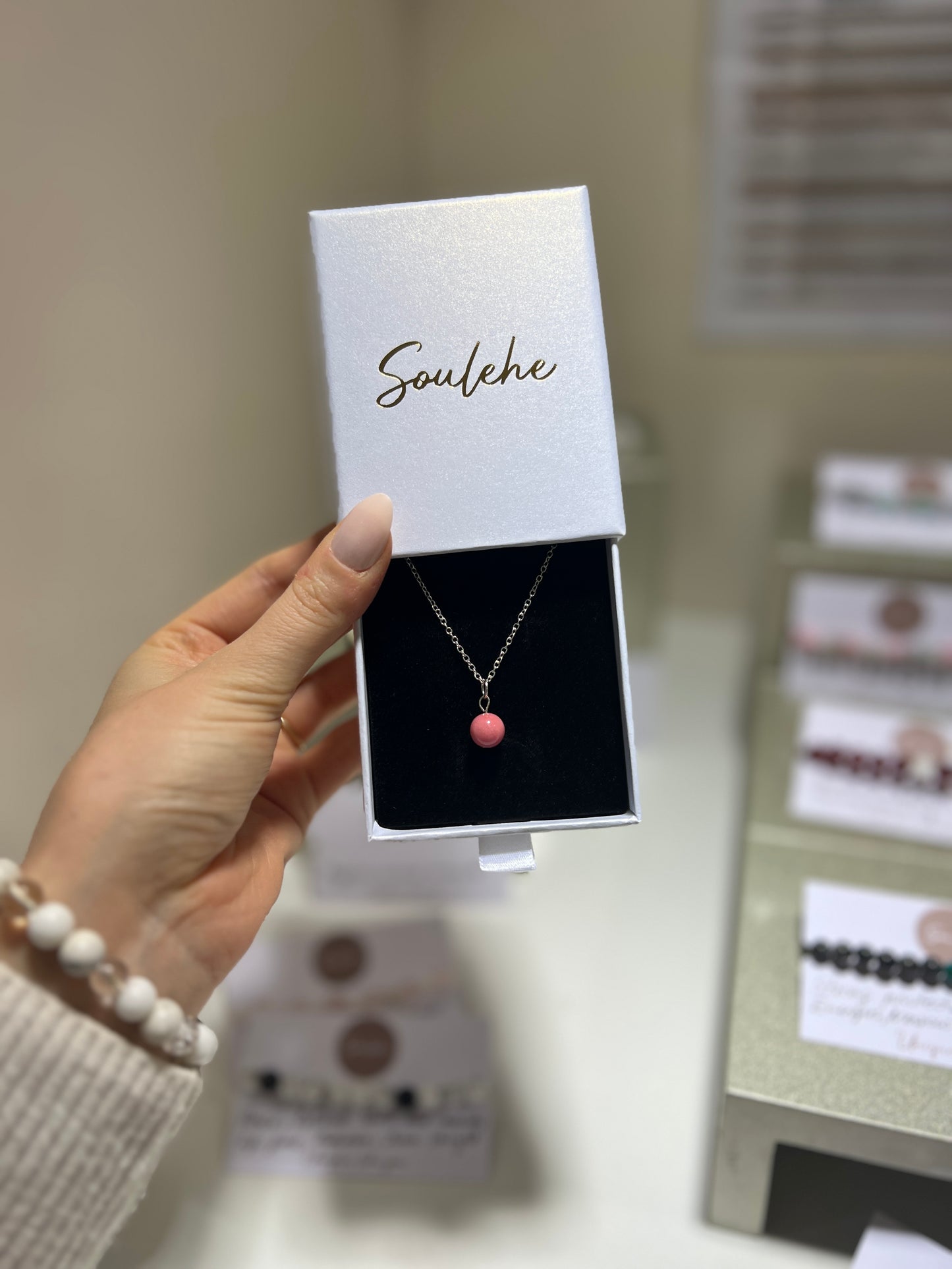 Necklace with a pink pendant held in front of a 'Soulehe' branded box.