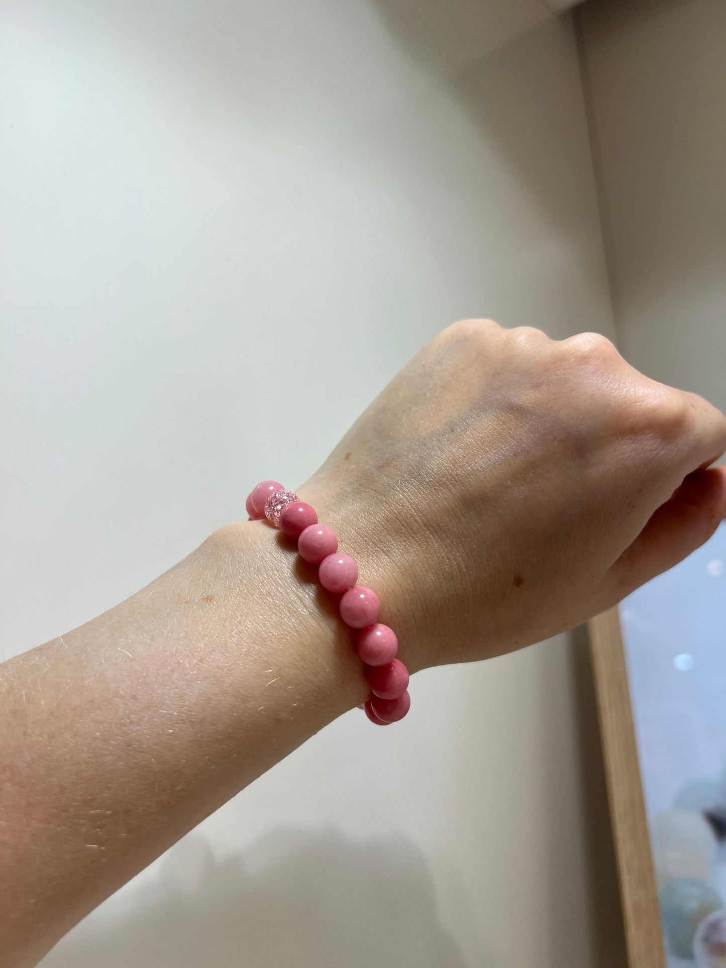 Hand wearing a pink beaded bracelet on a light background