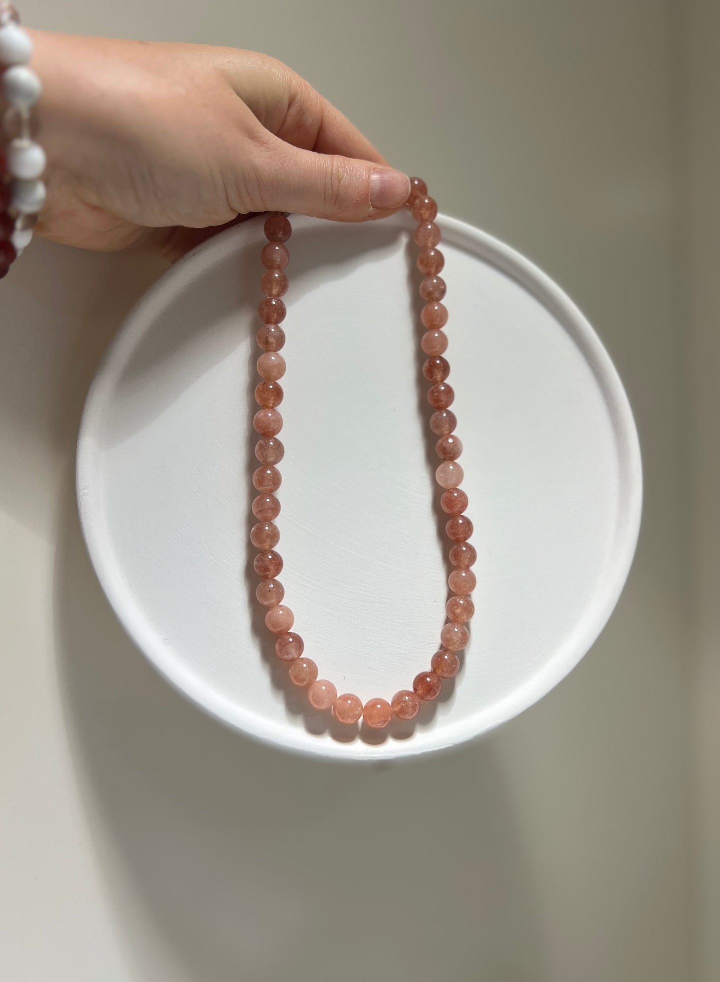 Necklace with pink beads on a white plate held by a hand against a neutral background