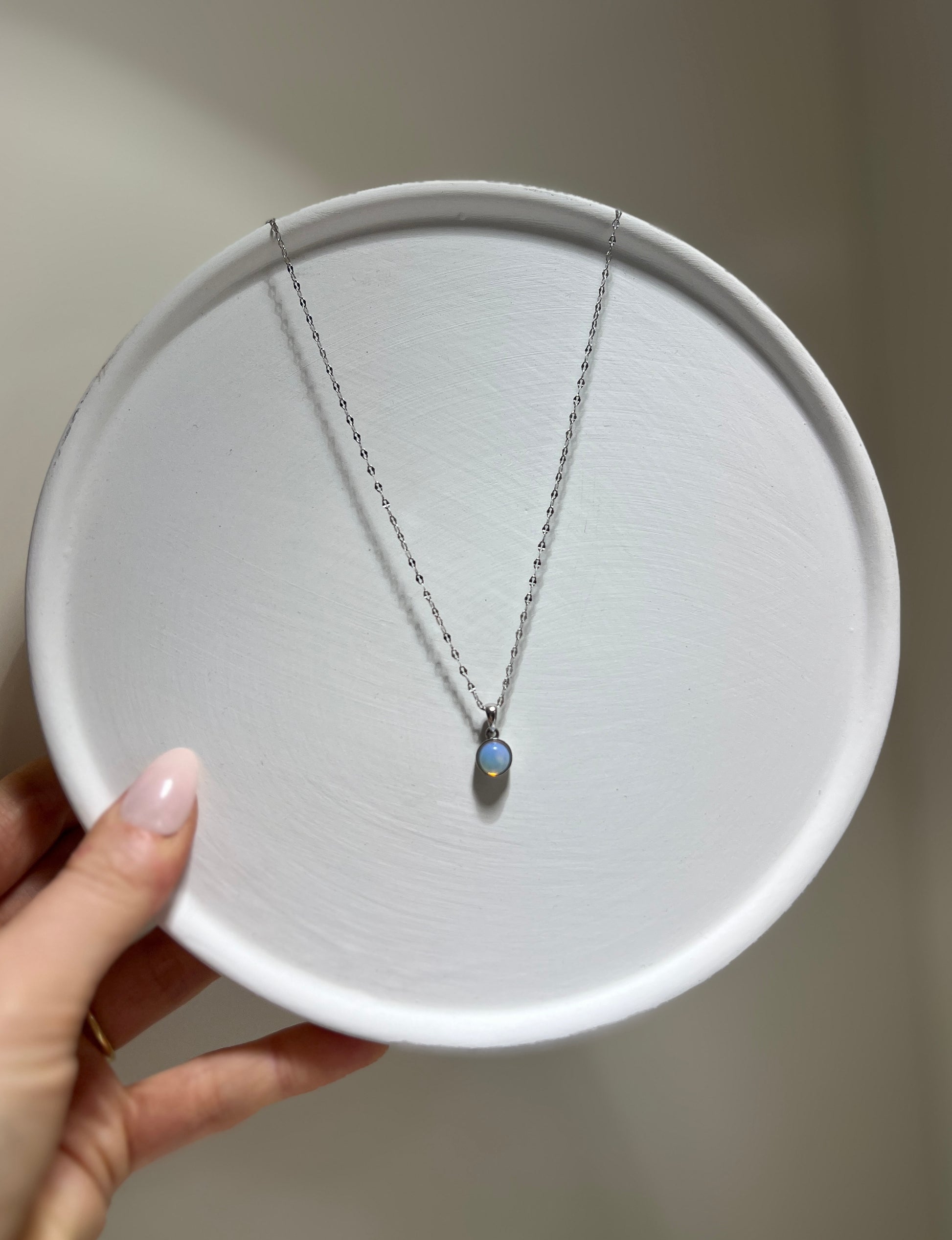 Necklace with a pendant on a white plate held by a hand against a neutral background