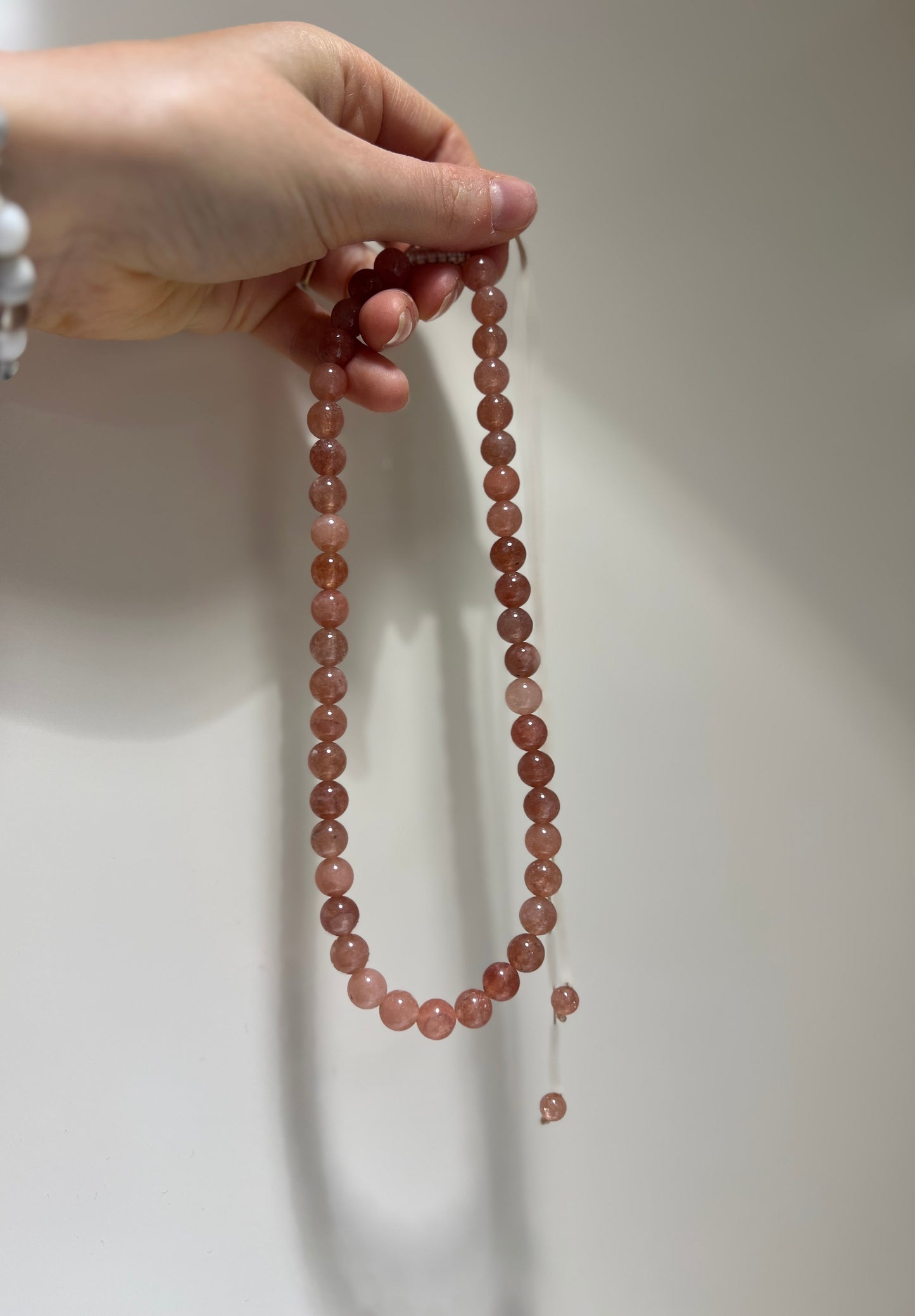 Hand holding a string of pink beads against a neutral background