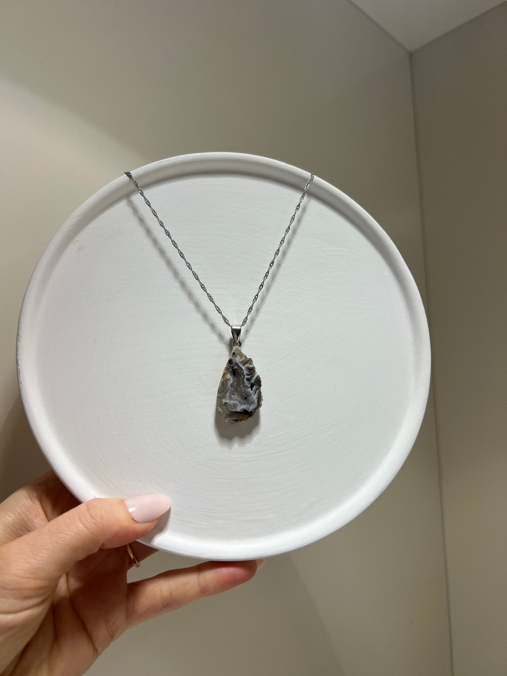 Necklace with a pendant on a white plate held by a hand against a neutral background