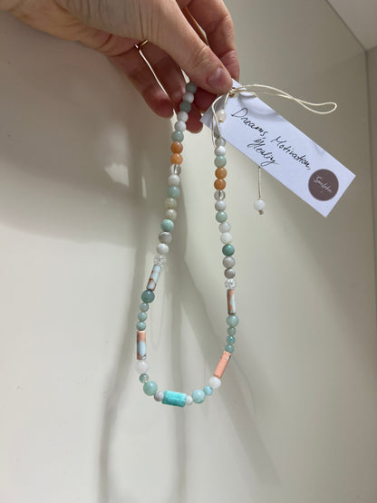Beaded necklace held by a hand with a visible brand tag on a light background