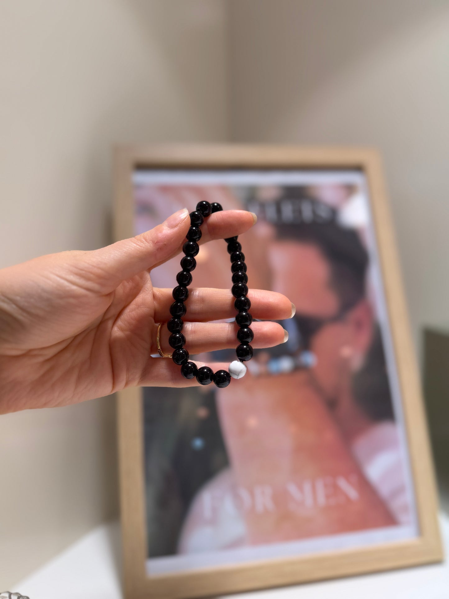 Hand holding a black beaded bracelet with a blurred photo in the background
