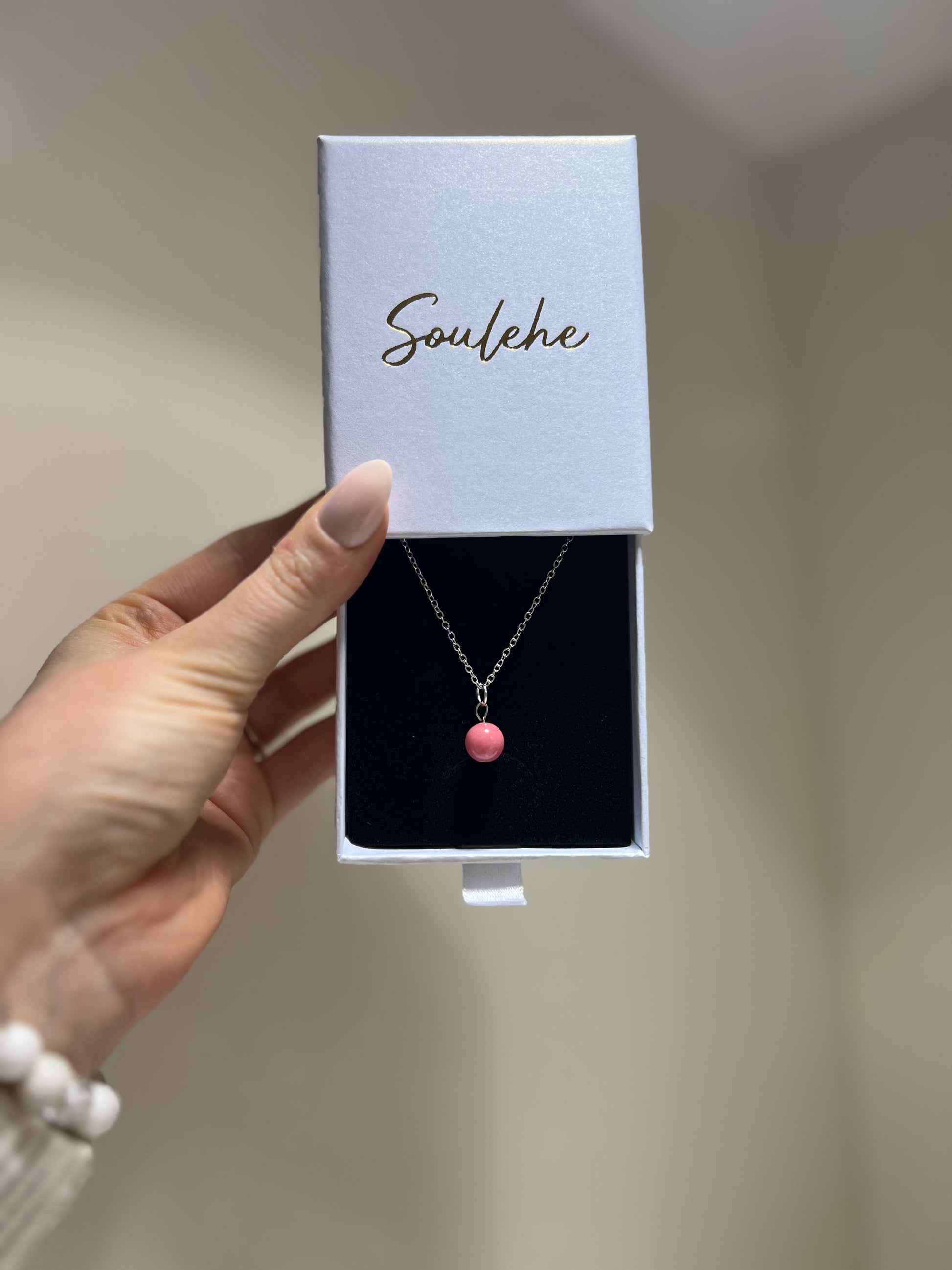 Necklace with a pink pendant in a 'Soulehe' box held by a hand.