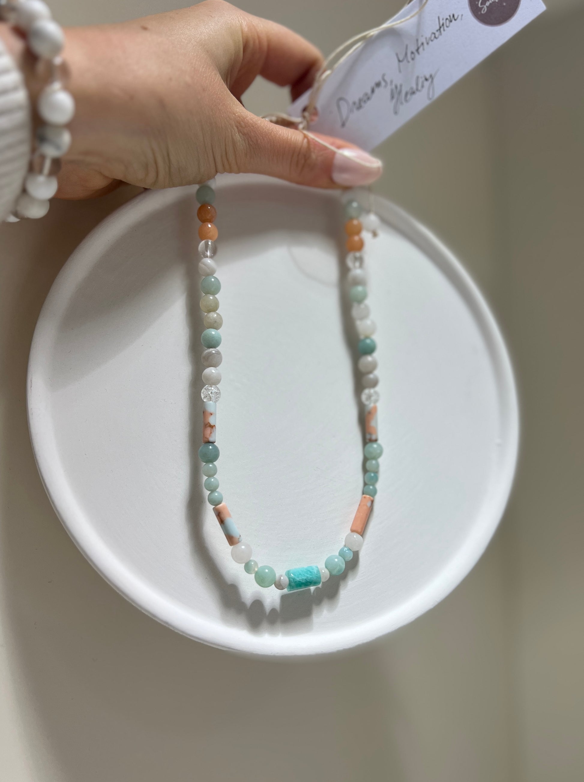 Beaded necklace on a white dish with a hand holding it, against a neutral background