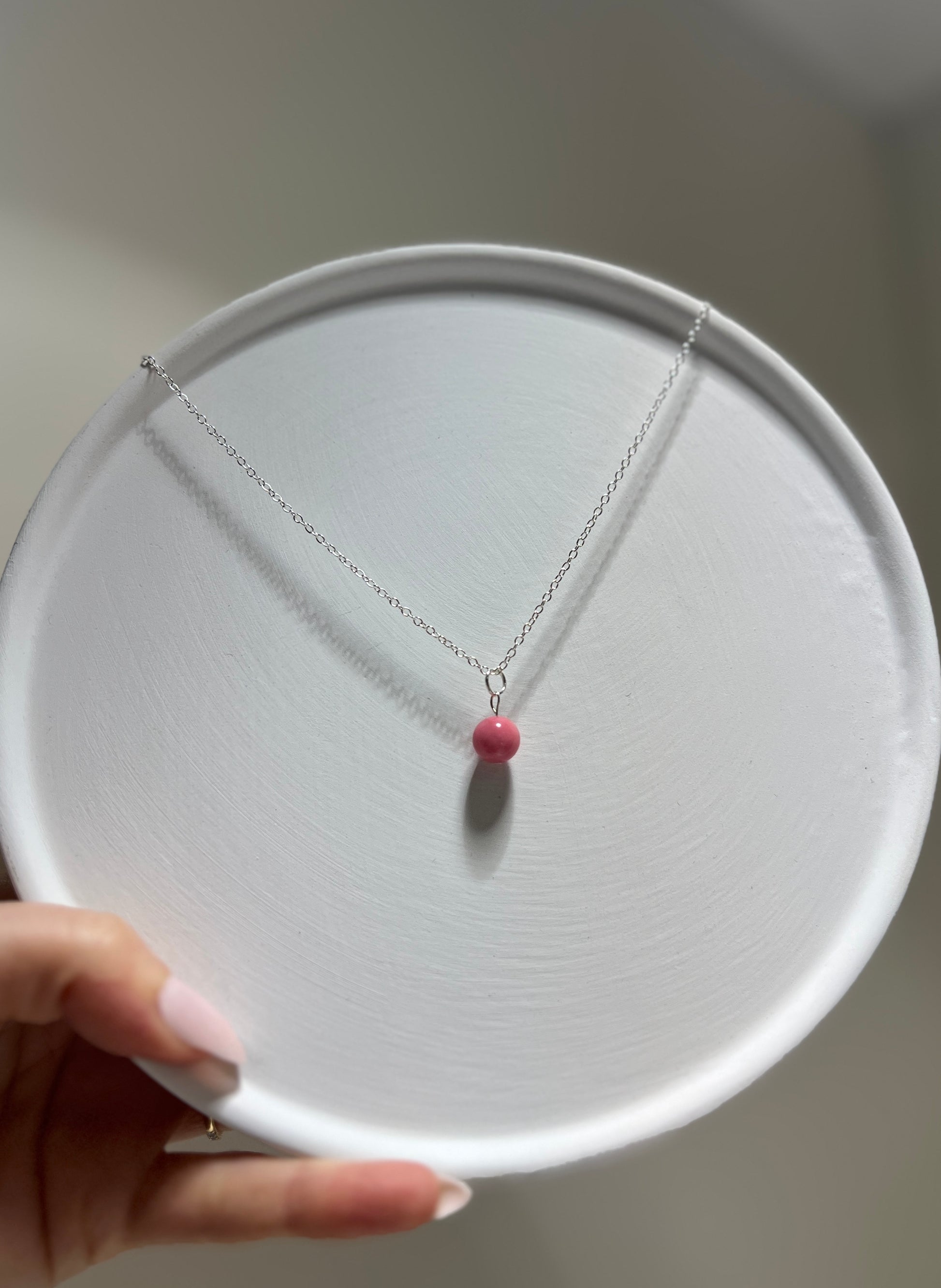 Necklace with a pink bead held on a white circular stand.