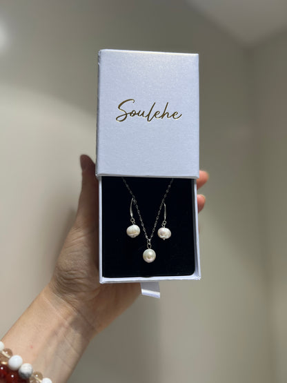 Pearl necklace and earrings set in a 'Soulehe' box held by a hand.