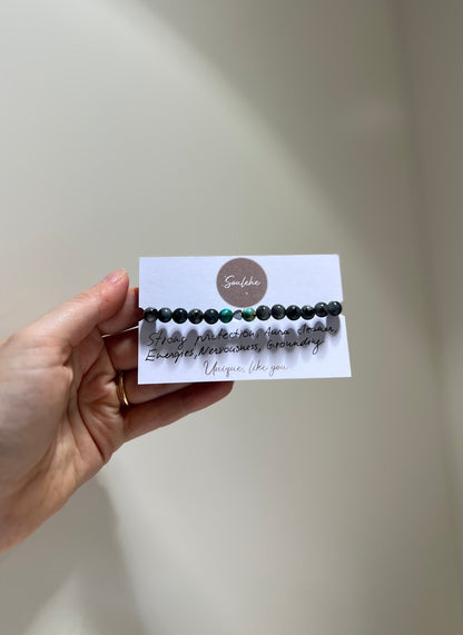 Hand holding a bracelet with a card featuring text and a logo against a neutral background