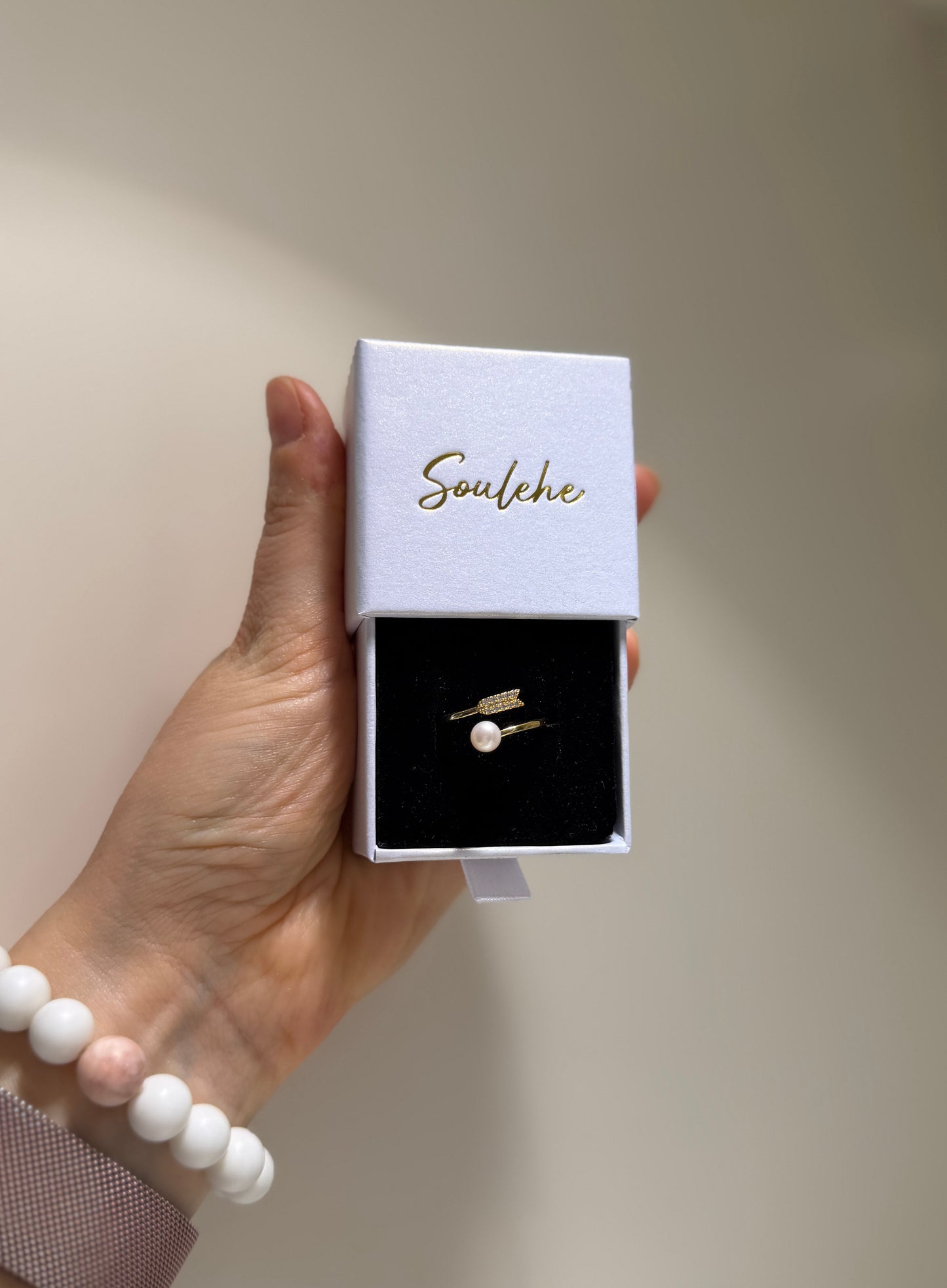 Hand holding a box with a pearl ring inside, branded 'Soulehe'.