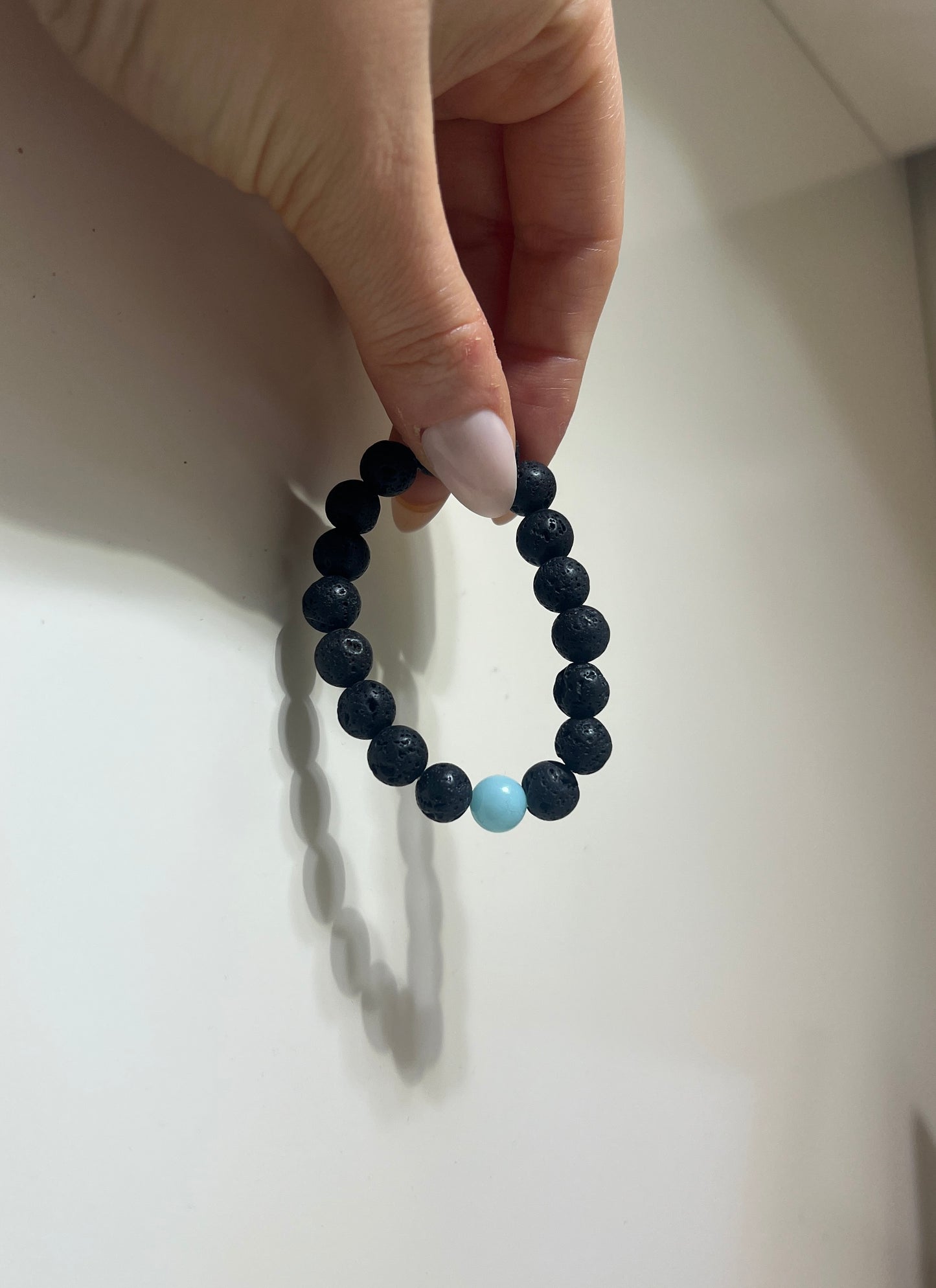 Black beaded bracelet with a turquoise bead held by a hand on a light background
