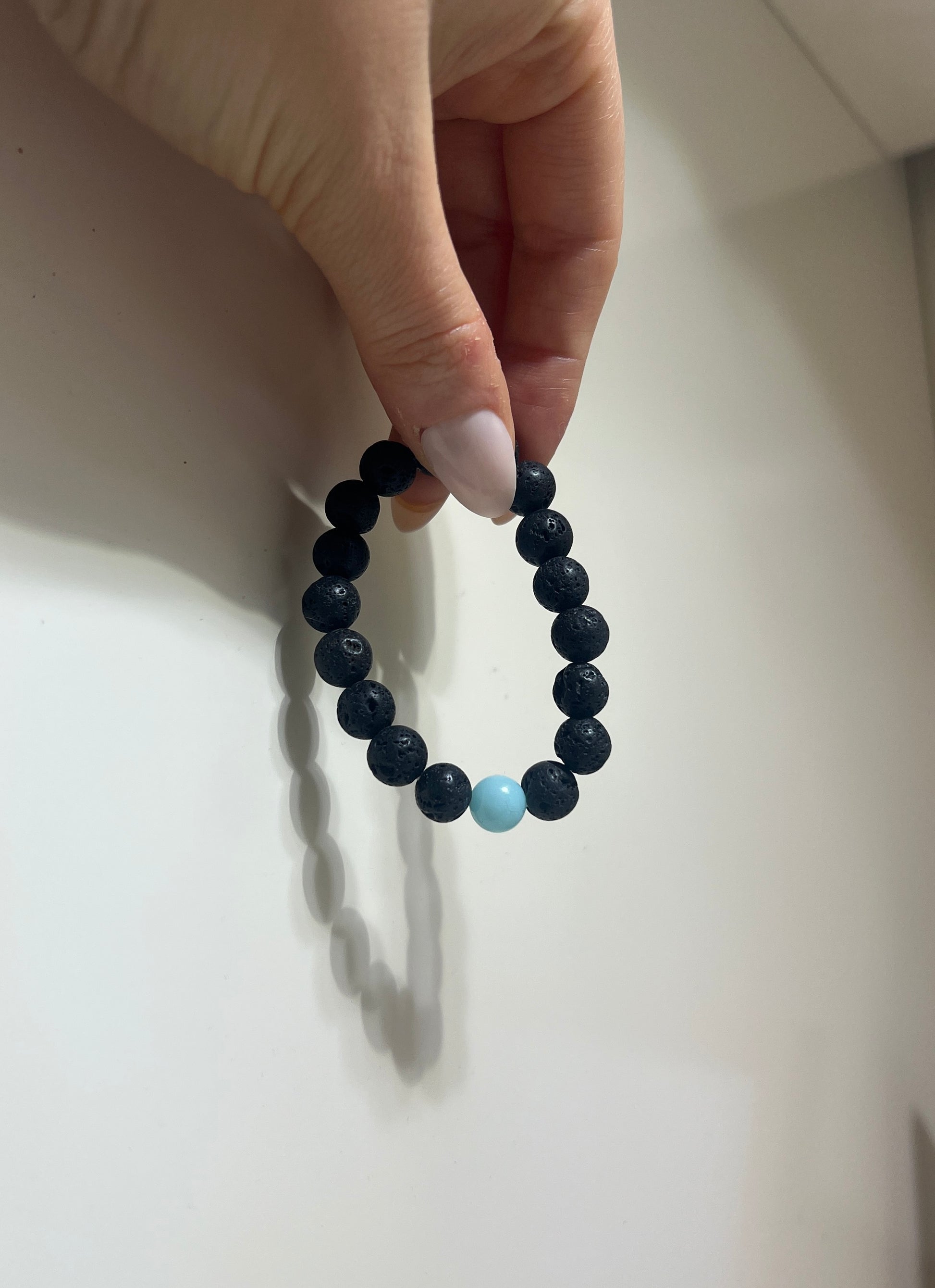 Black beaded bracelet with a turquoise bead held by a hand on a light background