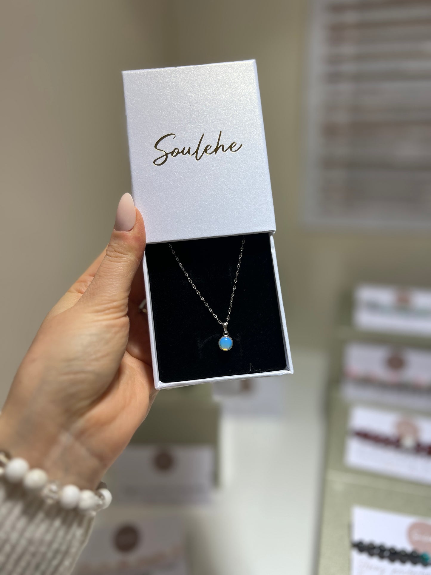 Hand holding a necklace in a 'Soulehe' box with blurred jewelry store background