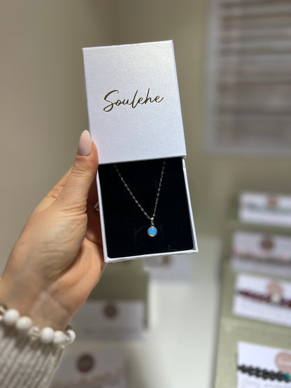 Hand holding a necklace in a 'Soulehe' box with blurred jewelry store background