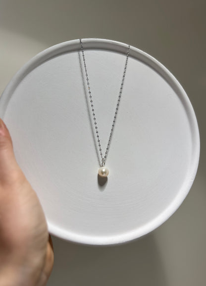 Pearl necklace on a white plate held by a hand