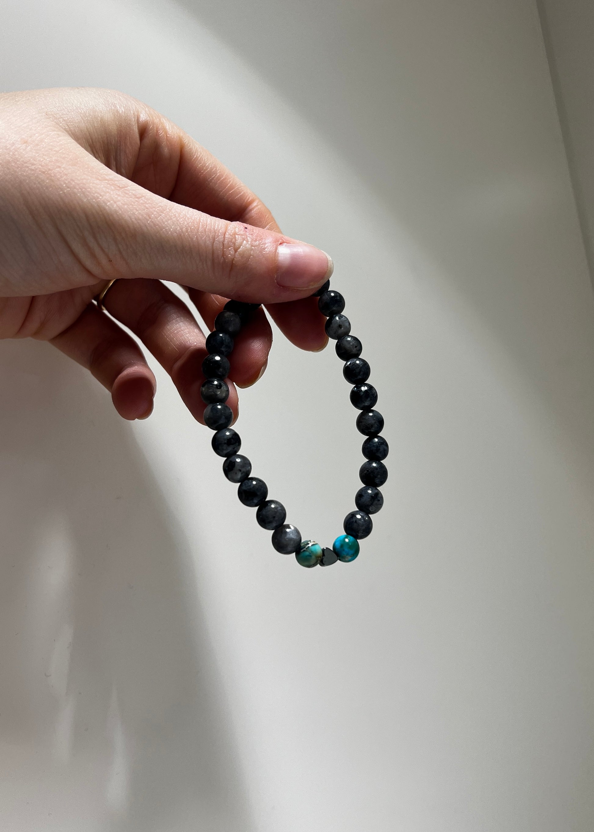 Hand holding a black beaded bracelet with a blue bead against a white background