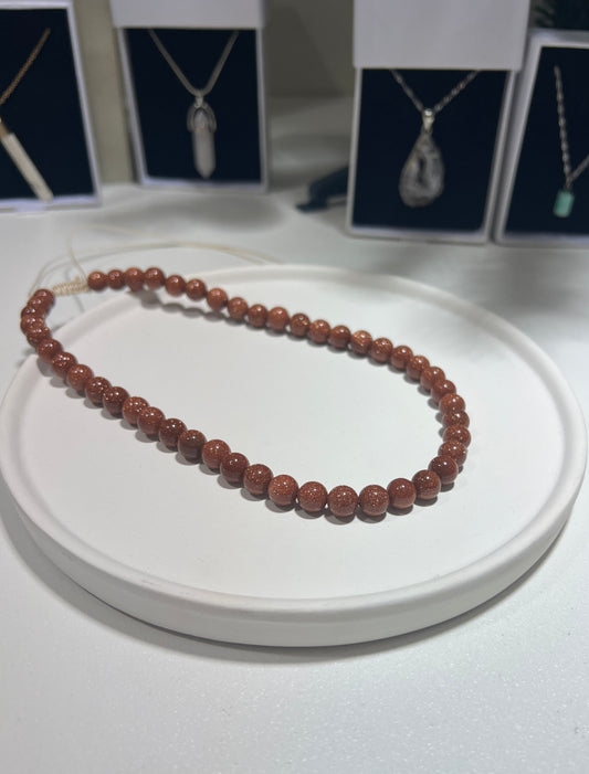 Brown beaded necklace on a white surface with jewelry displays in the background
