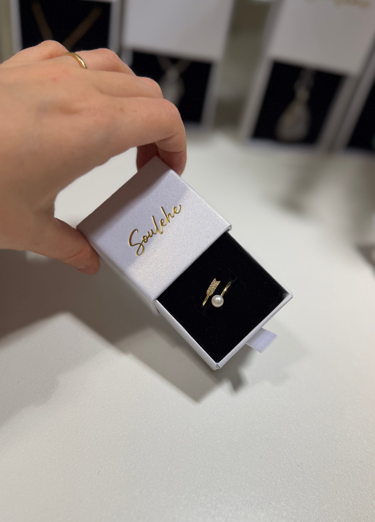Hand holding a jewelry box with a pearl earring inside, branded 'Soulehe'.