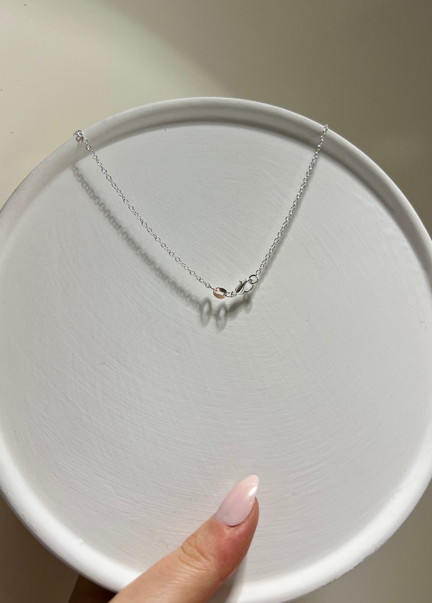 Silver necklace on a white plate held by a hand with pink nail polish.
