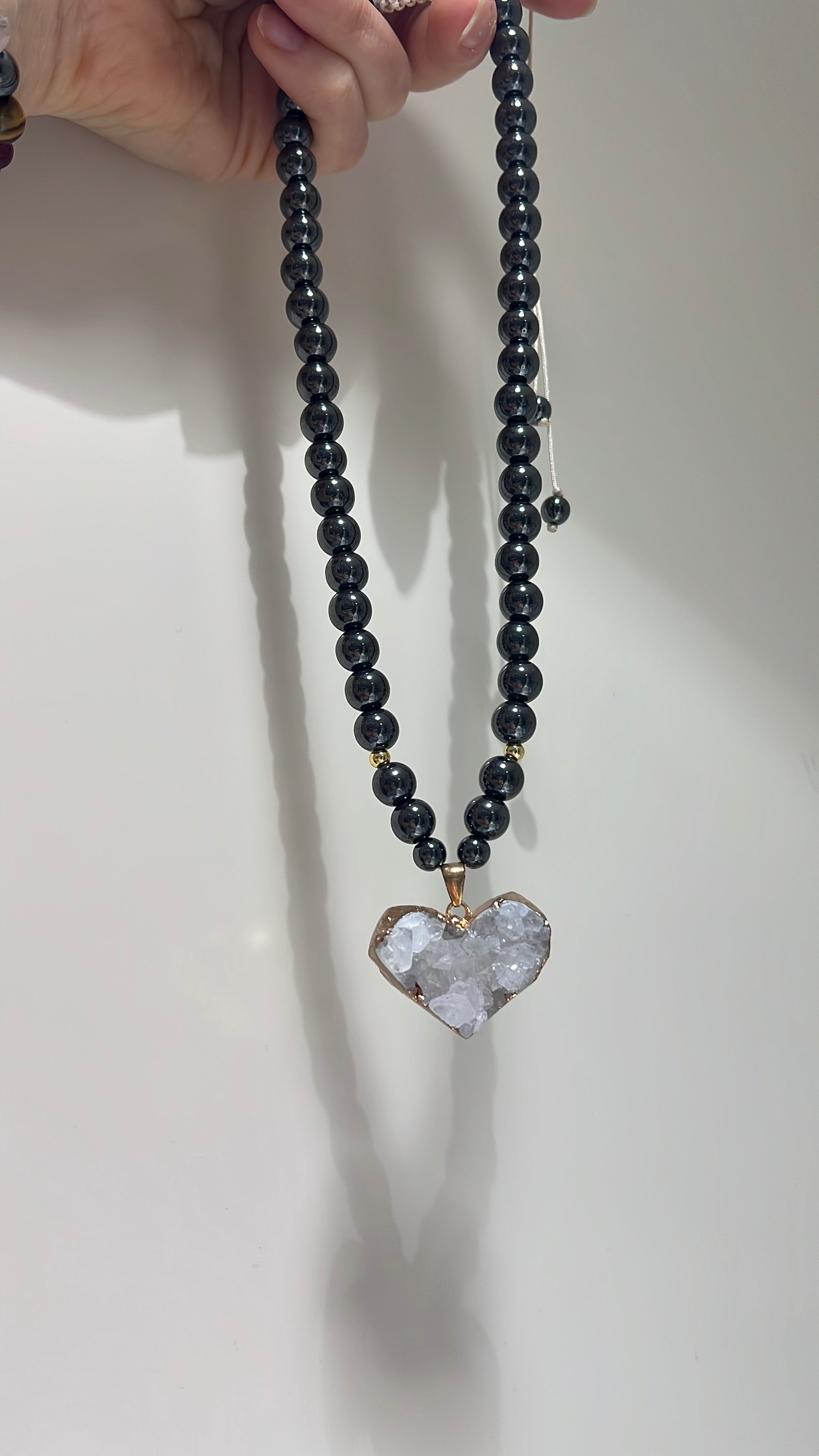 Necklace with a heart-shaped crystal pendant held by a hand on a white background