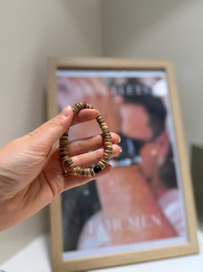Hand holding a beaded bracelet in front of a framed picture