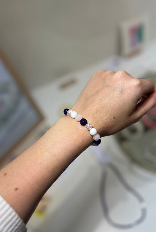 Person wearing a bracelet with purple and white beads on a blurred background