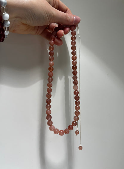 Hand holding a string of red beads against a white background