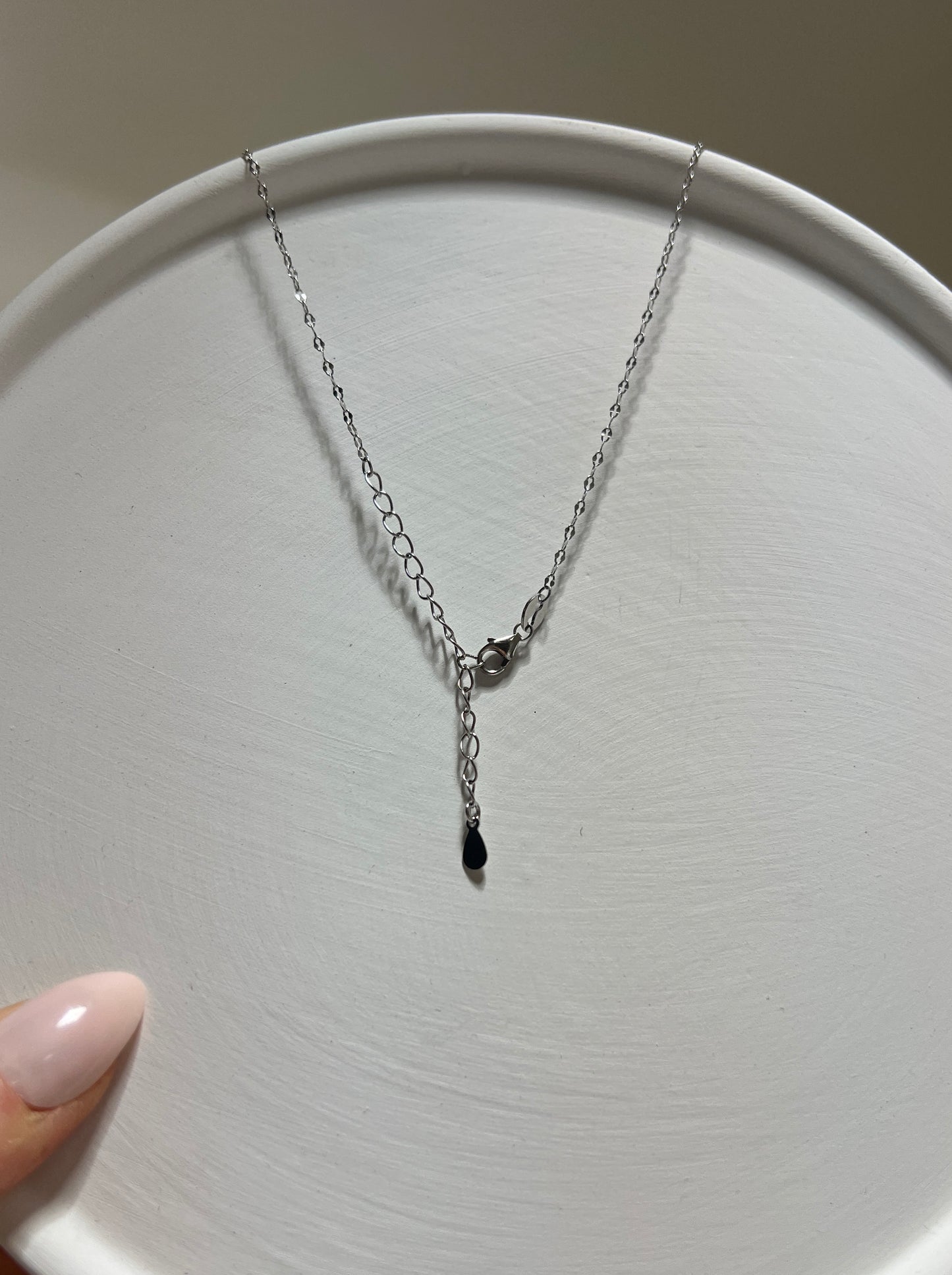 Silver necklace with a small black pendant on a white plate