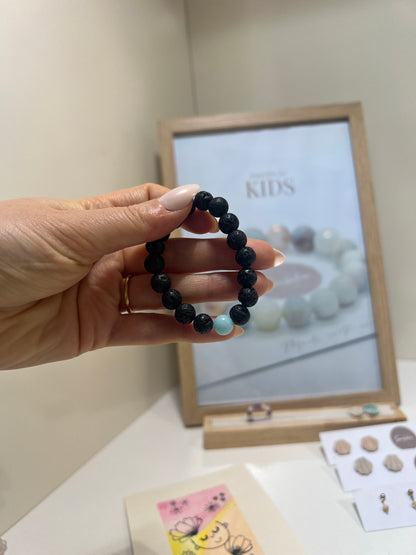 Hand holding a black beaded bracelet with a blurred background of jewelry and decor items.