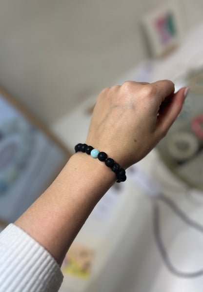 Hand wearing a black beaded bracelet with a blurred background