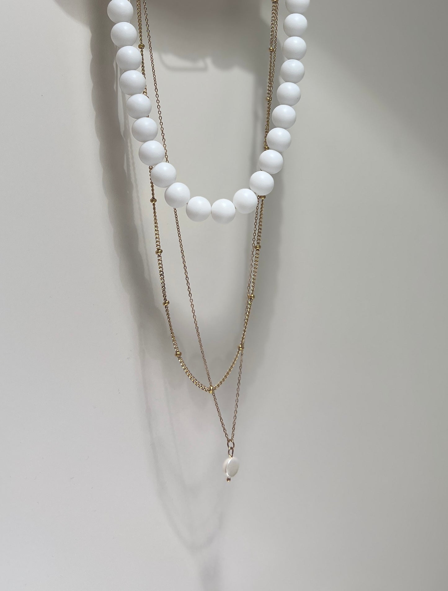 Two layered necklaces with white beads and gold chains on a white background