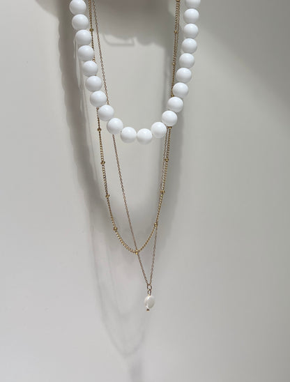 Two layered necklaces with white beads and gold chains on a white background