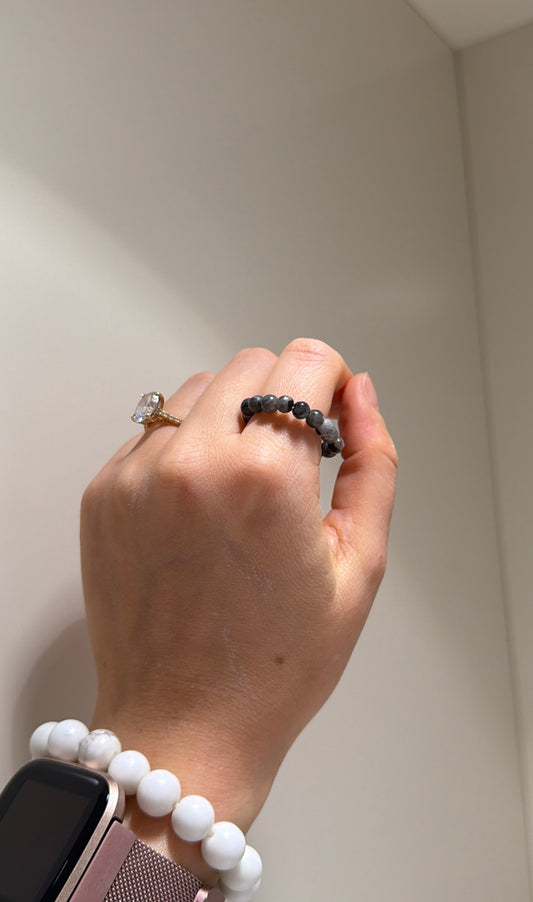 Hand wearing a ring and bracelet against a neutral background