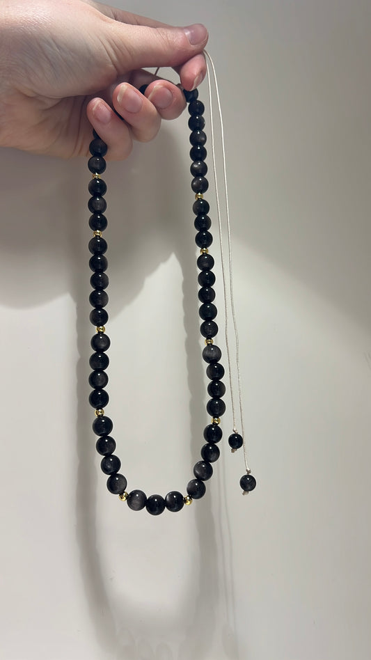 Black beaded necklace held by a hand against a plain background